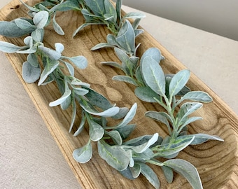 May include: A wooden tray with a light brown finish, filled with a garland of faux lamb's ear greenery. The leaves are a soft, silvery green color.