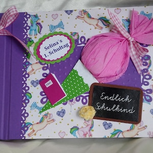 Könnte beinhalten: Lilafarbener Scrapbook mit einem rosa Band und einem weißen Einband mit einem Einhornmuster. Der Einband hat außerdem ein grünes und weißes Dreieck, ein rosa Bonbon und eine Kreidetafel mit dem Text "Endlich Schulkind".
