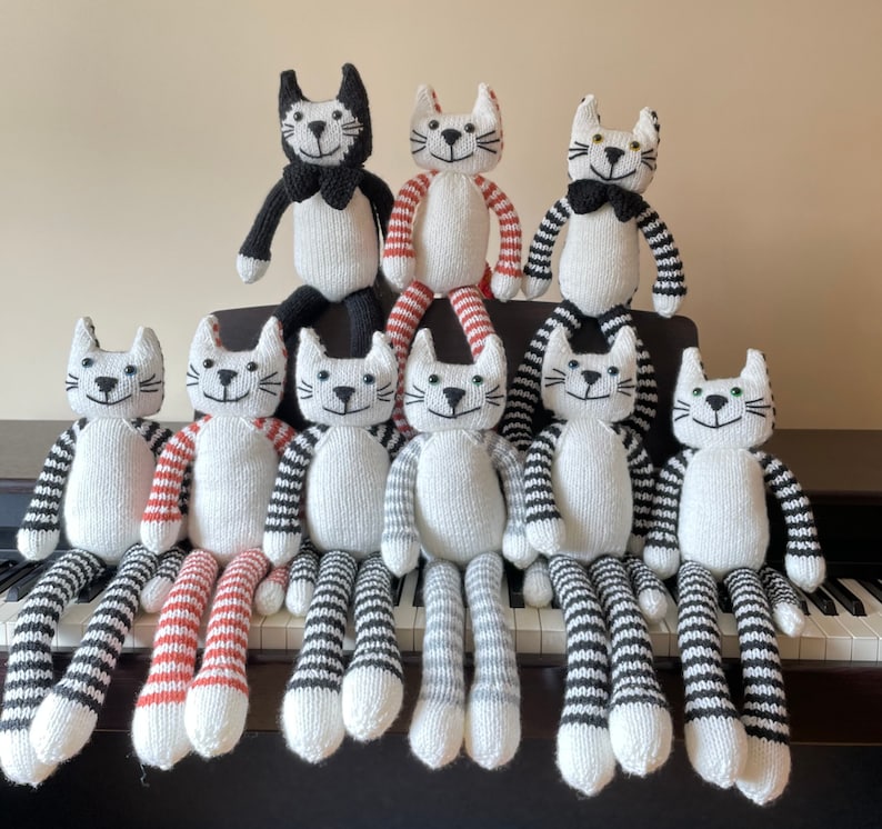 Puede incluir: Un grupo de nueve juguetes de gato tejidos en varios patrones en blanco y negro. Los gatos est&aacute;n todos sentados o de pie sobre una superficie con un teclado en el fondo.