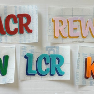 May include: Five different vinyl stickers with names written in colorful, bold, 3D letters. The names are ACR, REW, JJW, LCR, and KER.