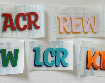 May include: Five different vinyl stickers with names written in colorful, bold, 3D letters. The names are ACR, REW, JJW, LCR, and KER.