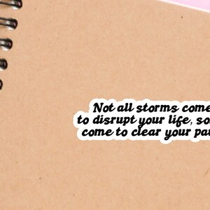 May include: A motivational quote sticker on a brown notebook. The quote reads: "Not all storms come to disrupt your life, some come to clear your path."