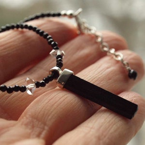 Op de afbeelding: Een zwarte ketting met een zilveren sluiting en een zwarte stenen hanger. De ketting is gemaakt van kleine zwarte kralen en heldere kristallen kralen.