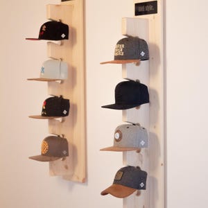 Könnte beinhalten: Baseballkappen-Präsentation auf Holzregalen an der Wand. Die Kappen sind in verschiedenen Farben erhältlich, darunter Schwarz, Grau und Braun, und weisen unterschiedliche Designs und Logos auf. Die Anzeige ist mit "mel style" und "mel cap" beschriftet.