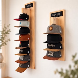 Könnte beinhalten: Zwei vertikale Wandhalterungen aus hellem Holz für Baseballkappen. Das linke Regal ist mit "mel cap." beschriftet und hält acht Kappen in verschiedenen Farben. Das rechte Regal trägt die Aufschrift "holy cap" und hält vier Kappen.