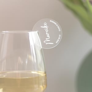 Könnte beinhalten: Ein Weinglas mit Weißwein, mit einem transparenten Getränkeanhänger aus Acryl. Der Anhänger trägt den Namen "Mareike" und die Namen "Susann & David" mit dem Datum "23.06.2024".