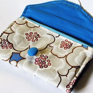 Könnte beinhalten: Eine handgefertigte Clutch mit einem Blumenmuster in Beige, Braun und Rosa. Der Innenraum und die Klappe sind hellblau. Sie hat einen blauen Knopfverschluss und einen blauen Reißverschluss.