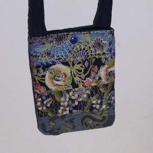 Könnte beinhalten: Eine kleine, rechteckige Umhängetasche mit einem dunkelblauen Riemen. Die Tasche besteht aus Stoffbahnen mit einem Patchwork-Design. Die obere Bahn ist blau mit einem Blumenmuster, die mittlere Bahn ist schwarz mit goldenen Akzenten und die untere Bahn ist grau mit einem Drachendesign.