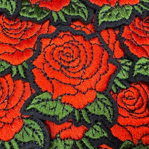 Puede incluir: Primer plano de parches bordados con rosas rojas con contornos negros y hojas verdes. Las rosas est&aacute;n densamente empaquetadas, creando un vibrante patr&oacute;n floral. Los parches son probablemente para fines decorativos.