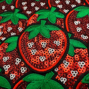 May include: Close-up of multiple red sequined strawberry patches with green leaves and black outlines. Each strawberry has white sequin seeds. The patches are likely for clothing or craft projects.