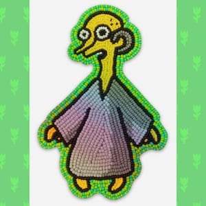 May include: A beaded character from the animated television show The Simpsons. The character is wearing a purple, blue, and green robe. The character has yellow skin, a large nose, and a single horn.