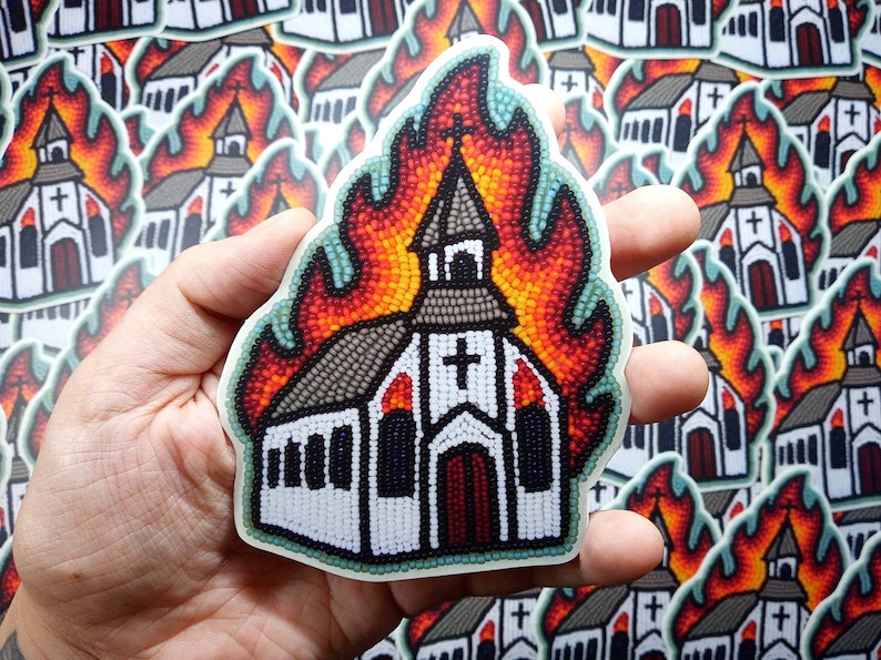 May include: A sticker featuring a church engulfed in flames. The church is white with a cross and a brown steeple. The flames are depicted in shades of red, orange, and yellow, with a beaded effect. The sticker is held in a hand.