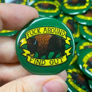 May include: Green button with a yellow and black bison and the text "F**k Around Find Out" in yellow letters.