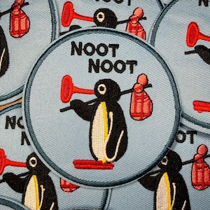 K&ouml;nnte beinhalten: Gestickter Aufn&auml;her mit einem Cartoon-Pinguin-Design. Der Pinguin hat einen roten P&ouml;mpel als Nase und tr&auml;gt eine rote Tasche. Der Text "NOOT NOOT" steht &uuml;ber dem Pinguin. Der Aufn&auml;her befindet sich auf hellblauem Hintergrund.