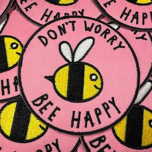 May include: Pink circular patch with the words "Don't Worry Bee Happy" embroidered in black. The patch features a yellow and black cartoon bee with a smiling face. The patches are stacked on top of each other.