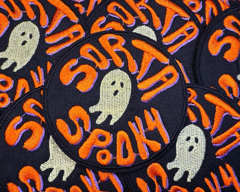 以下が含まれることがあります： 「SORTA SPOOKY」と書かれたオレンジ色の刺繍文字とゴーストグラフィックが特徴の黒い円形パッチ。テキストは紫色の輪郭です。ゴーストは白です。パッチは積み重ねられています。