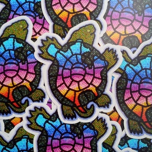Op de afbeelding: Een close-up van verschillende kleurrijke schildpad stickers. De schildpadden zijn gemaakt van een mozaïek van kleine, kleurrijke kralen. De stickers zijn in een willekeurig patroon gerangschikt.