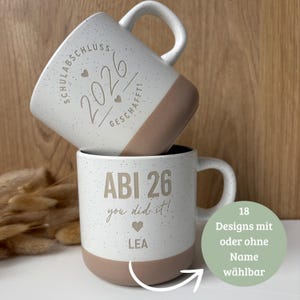 Könnte beinhalten: Zwei Keramiktassen mit gesprenkeltem weißem Oberteil und beigem Boden. Die obere Tasse zeigt den Text "SCHULABSCHLUSS 2026 GESCHAFFT!" mit Herzen. Die untere Tasse trägt die Aufschrift "ABI 26", "you did it!", ein Herz und den Namen "LEA".