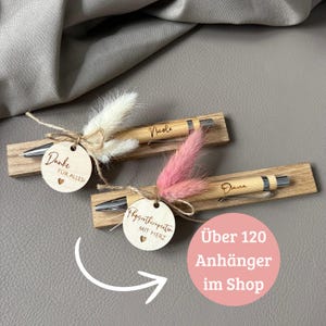 Könnte beinhalten: Zwei personalisierte Stifte mit Holzhaltern, jeweils verziert mit Trockenblumen und einem kleinen Holzanhänger. Ein Stift ist mit "Nicole" graviert, der andere mit "Diana". Die Anhänger lesen "Danke für alles!" und "Physiotherapeutin mit Herz."