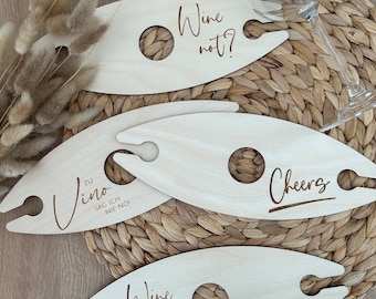 May include: Four wooden wine glass holders with different sayings. The sayings are "Wine not?", "Cheers", "Zu Vino Sag Ich Nie No!" and "Wine Time".