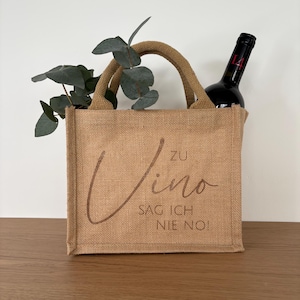 Könnte beinhalten: Eine braune Jute-Tragetasche mit einem braunen Ledergriff. Die Tasche hat den Text "Zu Vino Sag Ich Nie No!" in brauner Schrift auf der Vorderseite.