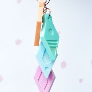 Peut inclure: Un porte-cl&eacute;s avec trois breloques&nbsp;: un diamant rose clair, un diamant bleu clair et un diamant turquoise clair avec une bande blanche. Les breloques sont attach&eacute;es &agrave; un anneau de cl&eacute; argent&eacute;.