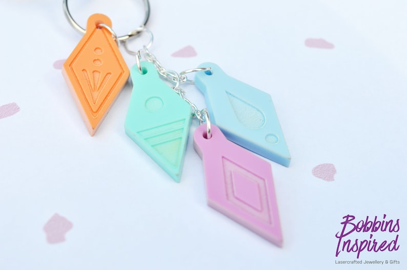 Peut inclure: Quatre porte-cl&eacute;s en forme de diamant de couleurs diff&eacute;rentes avec des motifs diff&eacute;rents. Les porte-cl&eacute;s sont attach&eacute;s &agrave; une cha&icirc;ne argent&eacute;e et &agrave; un anneau argent&eacute;. Les porte-cl&eacute;s sont orange, bleu clair, bleu et rose.