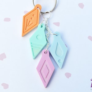 Peut inclure: Un porte-cl&eacute;s avec quatre breloques en forme de diamant de couleurs diff&eacute;rentes. Les breloques sont orange, bleu clair, bleu clair avec un motif de goutte blanche et rose. Le porte-cl&eacute;s est attach&eacute; &agrave; un anneau de cl&eacute; argent&eacute;.