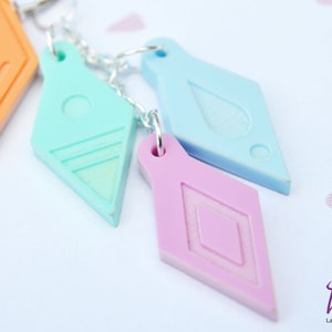 Peut inclure: Quatre breloques en forme de diamant de couleurs diff&eacute;rentes avec des motifs diff&eacute;rents, suspendues &agrave; une cha&icirc;ne argent&eacute;e. Les breloques sont dans des tons d'orange, bleu clair, turquoise et rose.