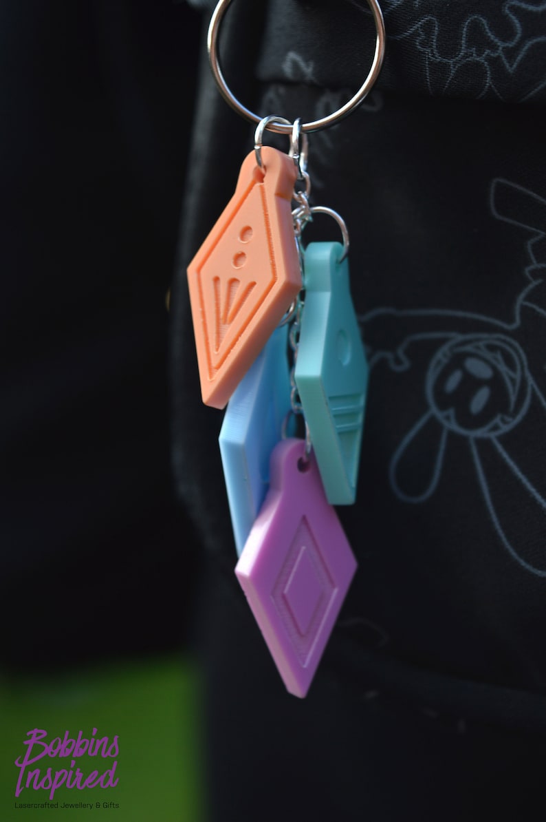 Peut inclure: Un ensemble de quatre porte-cl&eacute;s g&eacute;om&eacute;triques color&eacute;s. Les porte-cl&eacute;s sont en forme de diamants et sont en plastique. Les porte-cl&eacute;s sont attach&eacute;s &agrave; un anneau de cl&eacute; argent&eacute;.