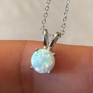 May include: A delicate silver necklace featuring a round, iridescent opal pendant. The opal is held in place by a four-prong setting, and the chain is a fine, linked design. The pendant is approximately 0.3 inches in diameter.
