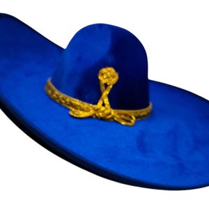 Op de afbeelding: Een levendige koningsblauwe sombrero met een brede, omhoogstaande rand en een hoge, ronde kroon. De hoed is versierd met een metallic gouden gevlochten bies rond de basis van de kroon, afgewerkt met een decoratief gouden knoopdetail aan de voorzijde.