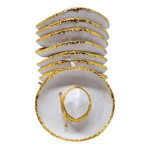 May include: A stack of white miniature sombreros featuring a wide brim and a pointed crown. Each hat is accented with a metallic gold braided trim along the edge of the brim and around the base of the crown. The hats are arranged vertically.