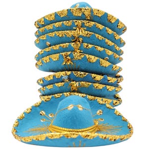May include: A stack of bright blue felt sombreros featuring gold metallic trim along the wide brims and crowns. Each hat is decorated with gold thread embroidery and gold sequins, with one hat positioned horizontally at the base of the vertical stack.