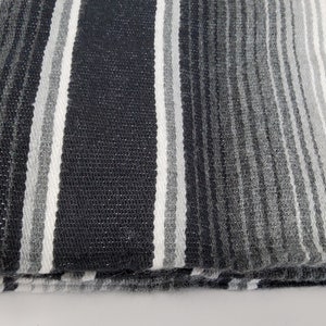 Peut inclure: Une couverture ray&eacute;e noire et blanche avec un d&eacute;grad&eacute; de rayures grises. La couverture est pli&eacute;e en deux et les bords sont effiloch&eacute;s.