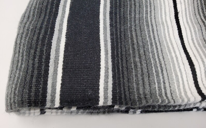Peut inclure: Une couverture ray&eacute;e noire et blanche avec un d&eacute;grad&eacute; de rayures grises. La couverture est pli&eacute;e en deux et les bords sont effiloch&eacute;s.