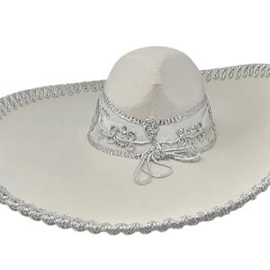 Op de afbeelding: Een witte sombrero met ingewikkeld zilverkleurig borduurwerk rond de kroon en een decoratieve zilveren gevlochten rand langs de brede, omhoogstaande rand. De hoed bevat een zilveren koorddetail aan de basis van de kroon voor een goede pasvorm.
