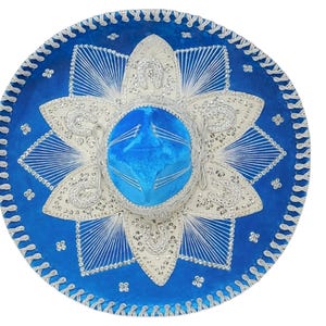 May include: A vibrant blue sombrero featuring intricate silver embroidery in a star-shaped pattern around the crown. The wide brim is decorated with silver thread detailing and small metallic accents, creating a textured, ornate appearance.