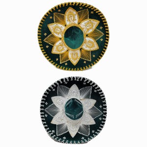 Op de afbeelding: Twee groene fluwelen sombreros met gouden en zilveren borduurwerk. De sombreros hebben een traditioneel ontwerp met een bloemenpatroon.