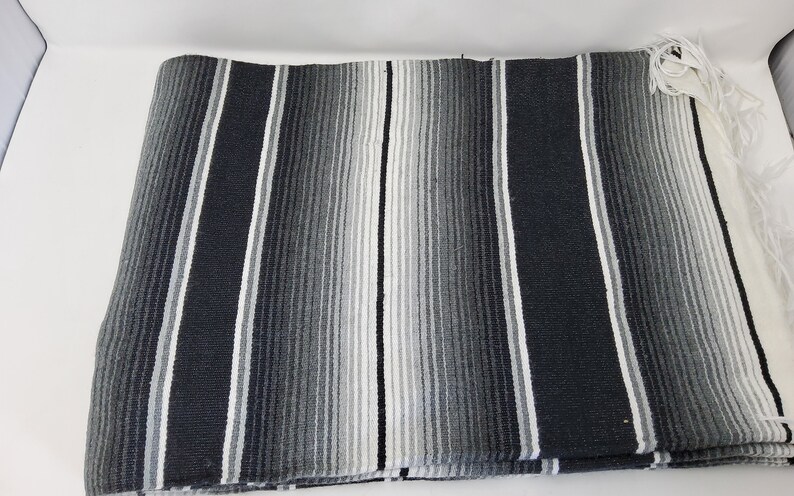 Peut inclure: Une couverture ray&eacute;e noire et blanche avec une bordure en franges. La couverture est faite d'un tissu doux et tiss&eacute;.