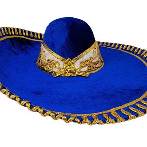 May include: A vibrant royal blue sombrero featuring a wide brim and a rounded crown. The hat is decorated with intricate gold metallic trim along the edge and a white band around the base of the crown, accented with detailed gold embroidery.