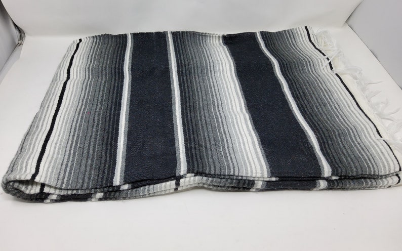 Peut inclure: Une couverture mexicaine &agrave; rayures noires et blanches avec des franges sur les bords.