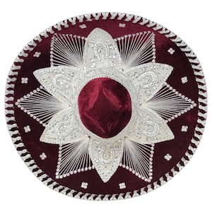 Peut inclure: Un sombrero en velours bordeaux profond orné de broderies métalliques argentées complexes en forme d'étoile autour de la calotte. Le large bord est décoré de détails en fil d'argent, de petits accents argentés et d'une bordure tressée.