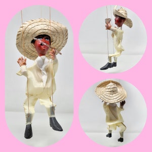 Könnte beinhalten: Eine Vintage-Handpuppe mit einem Strohhut, einem weißen Hemd und einer braunen Hose. Die Puppe hält ein kleines Holzinstrument in der Hand.