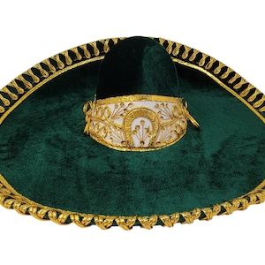 May include: A dark green velvet sombrero featuring a wide brim with gold braided trim along the edge. The crown is accented with a white band decorated with gold embroidered floral patterns and a prominent gold horseshoe design at the center.