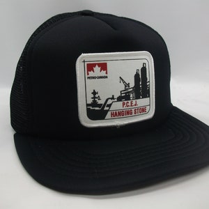 May include: Black trucker hat with a white patch featuring a black and white illustration of an oil refinery with the text "P.C.E.J. HANGING STONE" and a red Canadian flag with the text "PETRO CANADA".