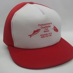 May include: A red and white trucker hat with the text "Poissonnerie Ouellette Fish Market Atholville. N.B. (506) 753-7168" printed on the front. The hat features a red fish and a lobster illustration.
