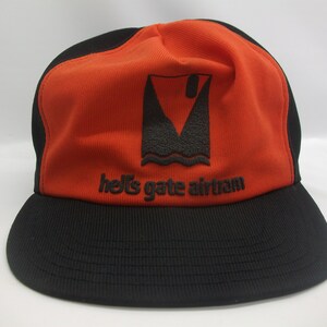 May include: A black and orange baseball cap with a black logo that says "hell's gate airteam" and a graphic of a boat with a sail.