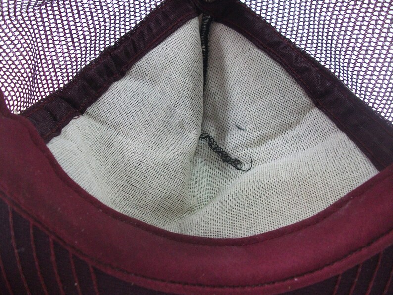 May include: The inside of a burgundy mesh trucker hat. The hat has a white cotton lining and a burgundy brim.