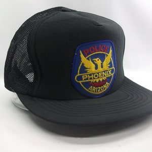 May include: Black mesh trucker hat with a blue, red, and yellow embroidered patch that says "Police Phoenix Arizona".